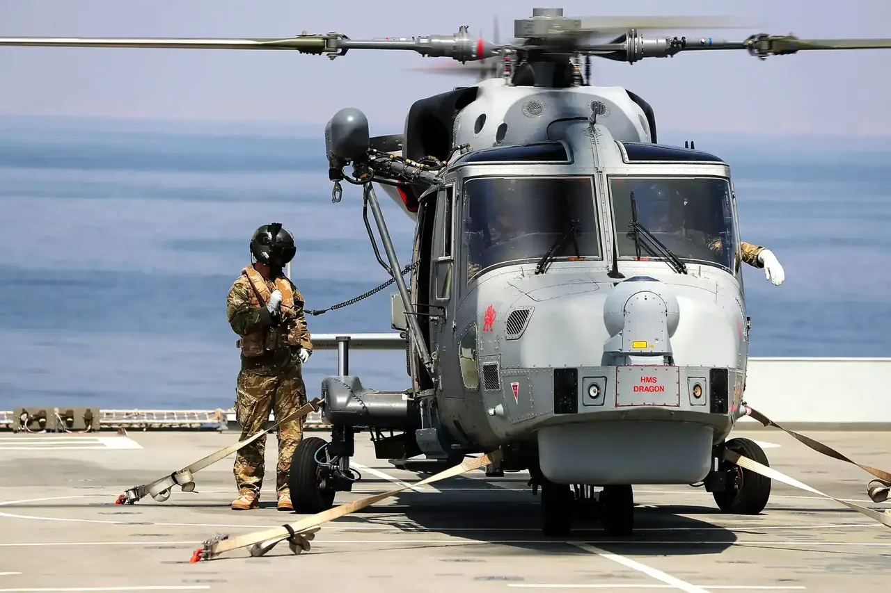 A military helicopter on the deck of an aircraft carrier with the crew completing walkaround checks.