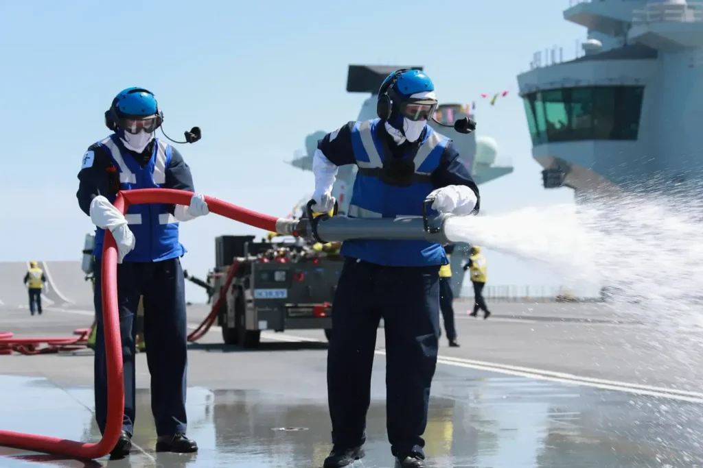 Crew members completing a crash exercise drill on an aircraft carrier by operating a water hose.