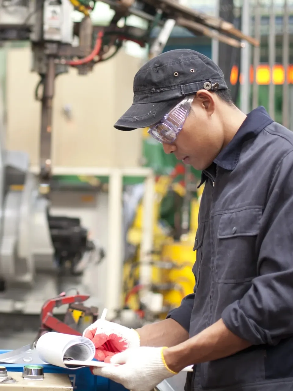 A man working in a factory with safety gear on and completing a checklist.