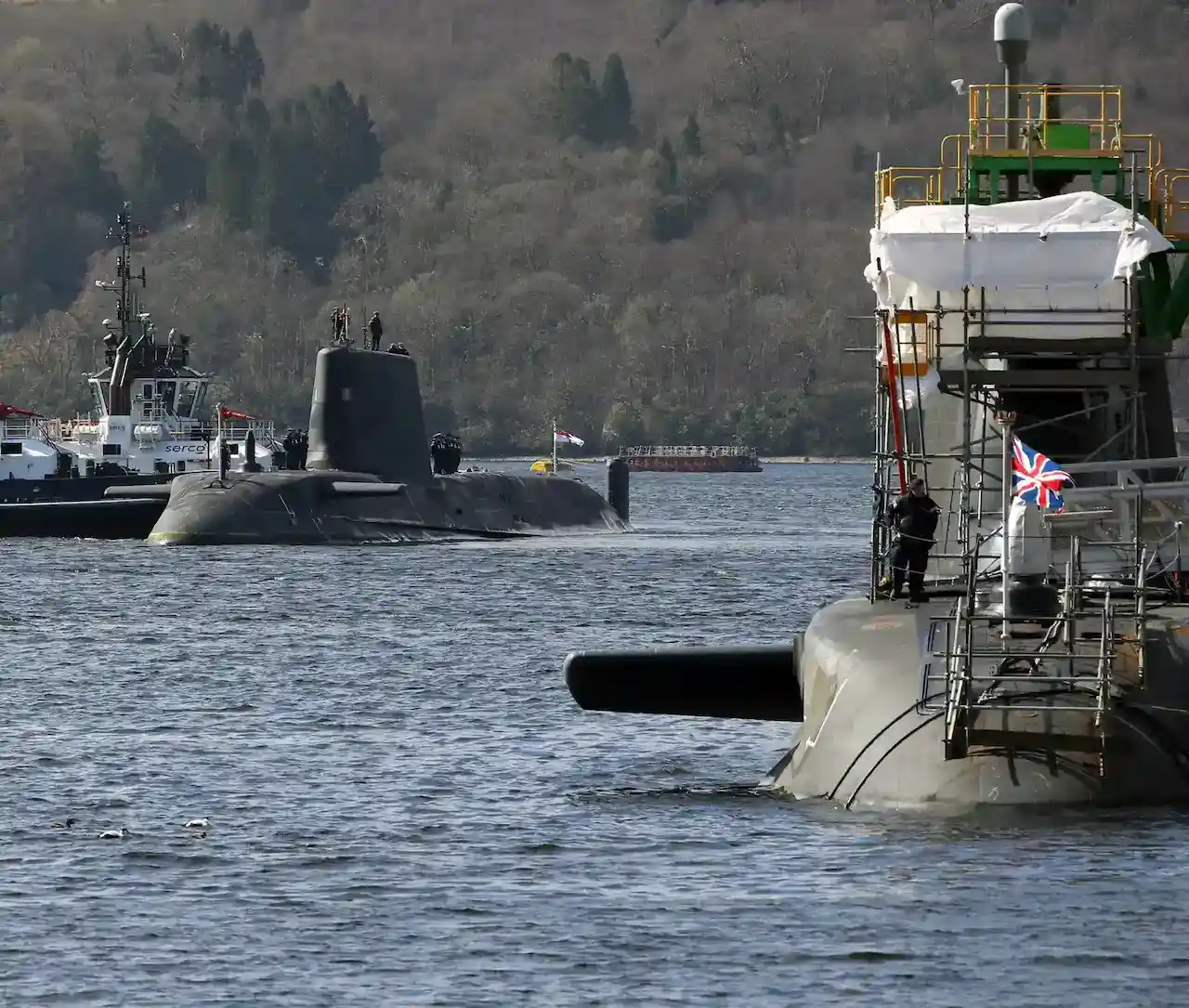 Two submarine that have surfaces, one with maintenance being completed and the other with a small boat next to it.