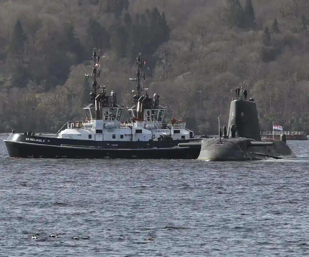 A surfaced submarine with a small ship next to it.