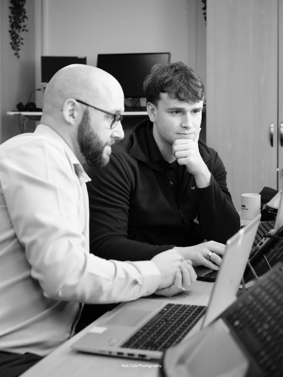 Two people sat next to each other, working on laptops.