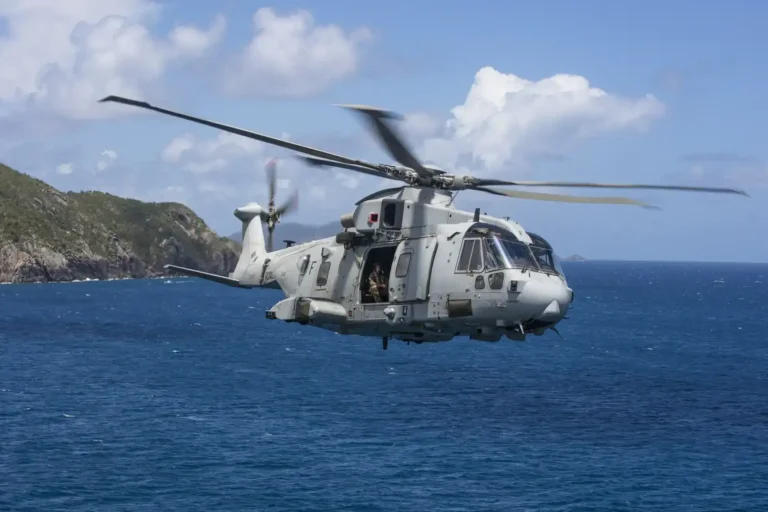 A military helicopter flying over blue seas with mountains in the background.