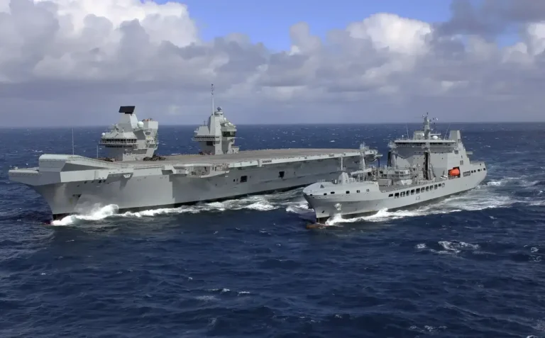 A large military aircraft carrier side-by-side with another military ship, sailing through the sea.