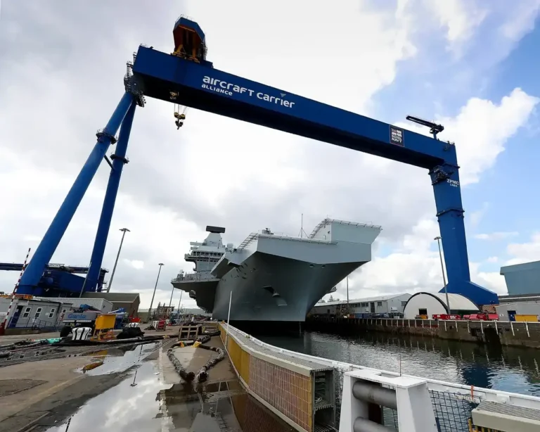 A large military ship in a dry dock with a large crane over the top of it.