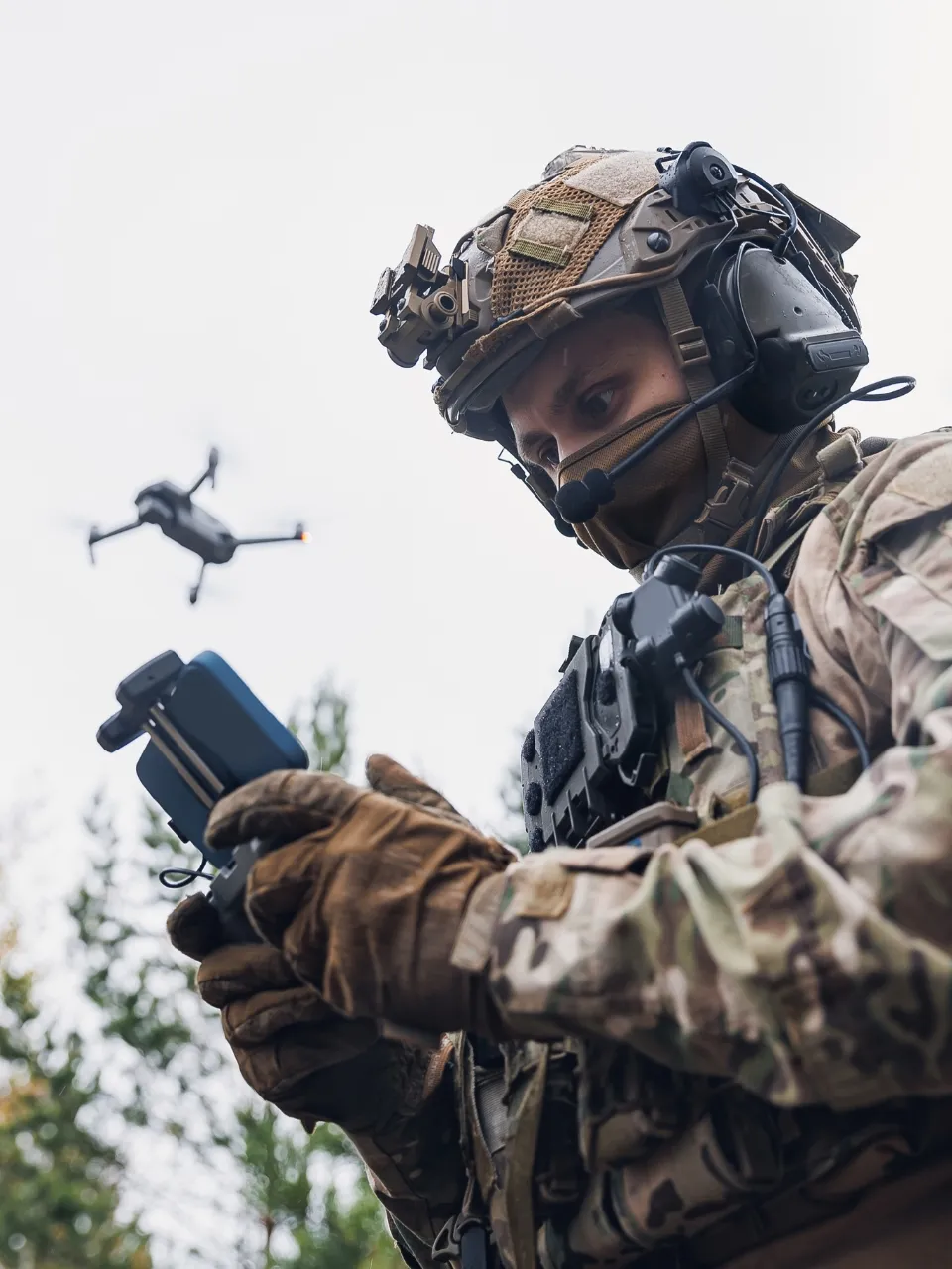 A soldier operating an remotely piloted air system with the drone in the background above their head.