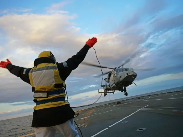 An operator signalling to a helicopter as it lands on a ships deck.