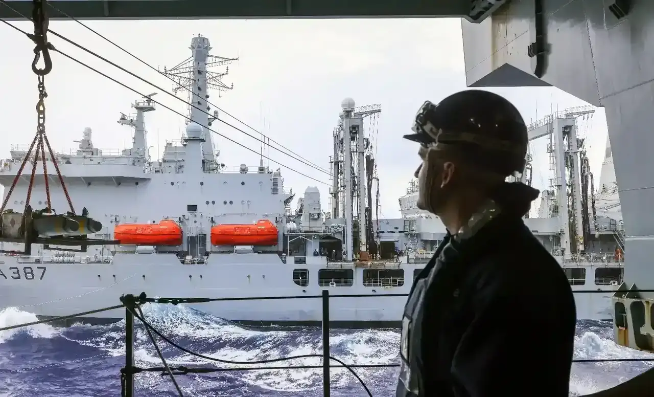 A crew member looking at munitions being transfered to an adjacent ship.