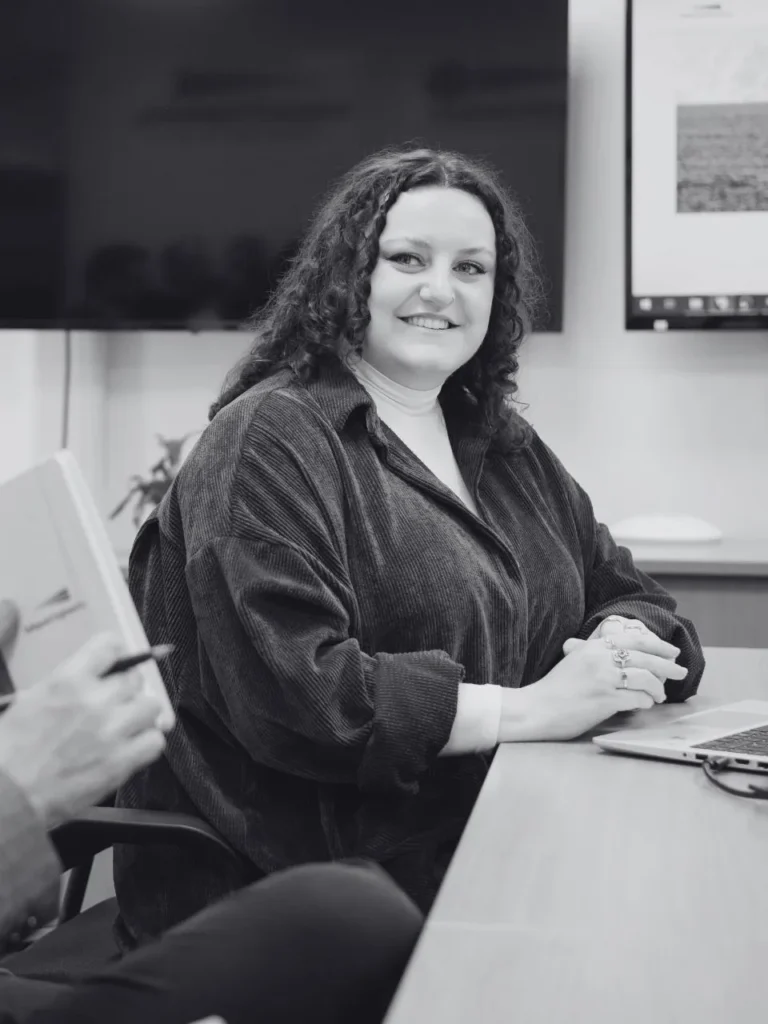 A woman sat at a meeting table with her hands together and smiling.